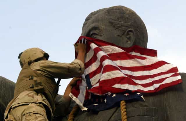 A U.S. Marine covers the face of a statue of Iraqi President Saddam Hussein with a U.S. flag in Baghdad, on April 9, 2003. U.S. troops briefly draped an American flag over the face of a giant statue of Hussein, as they prepared to topple it in front of a crowd of Iraqis. (Photo by Goran Tomasevic/Reuters/The Atlantic)