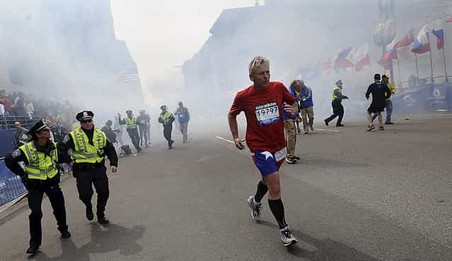 A Boston Marathon competitor and Boston police run from the area of an explosion near the finish line in Boston, Monday, April 15, 2013. (Photo by Ken McGagh/AP Photo/MetroWest Daily News)