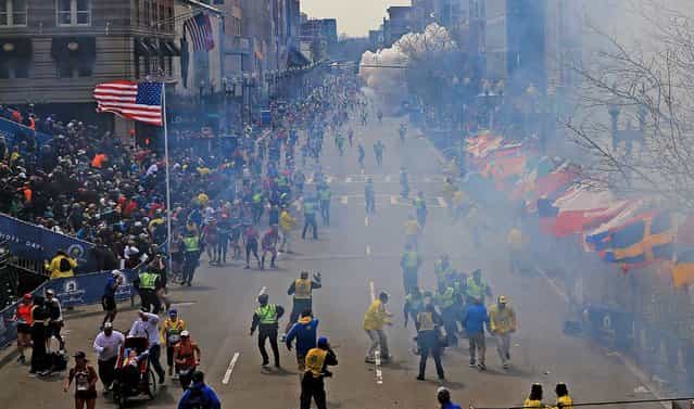 Moments after the first explosion near the finish line of the Boston Marathon, smoke is seen in the background where a second explosion occurred. (Photo by David L. Ryan/The Boston Globe)