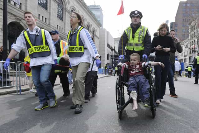 A Boston police officer wheels in injured boy down Boylston Street as medical workers carry an injured runner following an explosion during the 2013 Boston Marathon in Boston, Monday, April 15, 2013. (Photo by Charles Krupa/AP Photo)