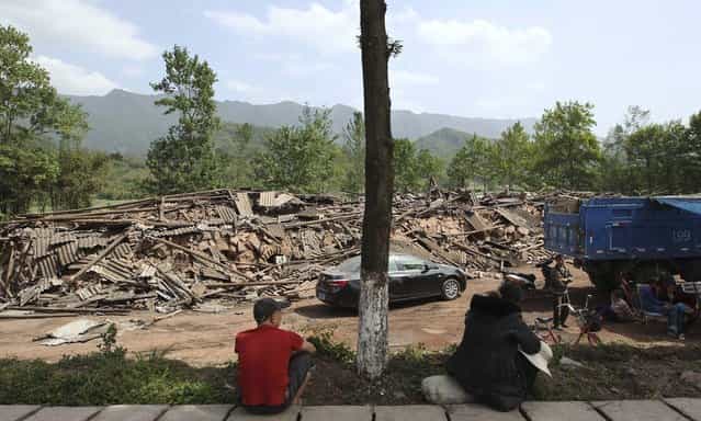 People sit near collapsed buildings after a strong 6.6 magnitude earthquake, at Longmen village, Lushan county, Ya'an, Sichuan province, April 20, 2013. (Photo by Reuters/Stringer)