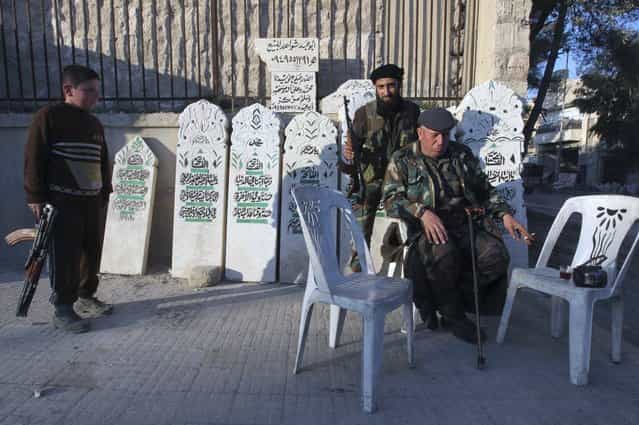 A boy carries a weapon as he stands next to Free Syrian Army Fighters in front of gravestones in Aleppo January 15, 2013. (Photo by Muzaffar Salman/Reuters)