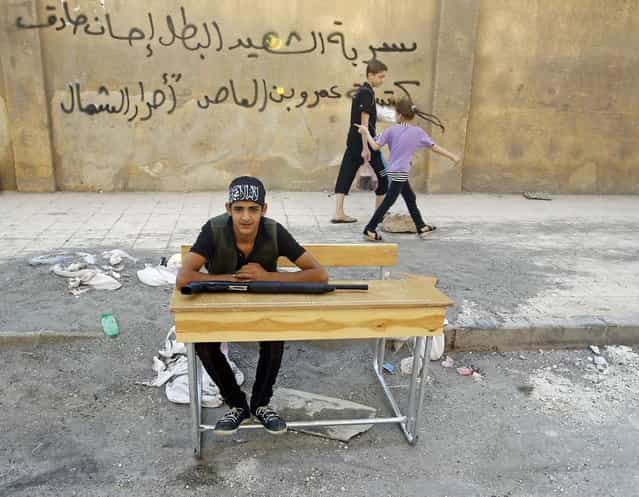 A young Free Syrian Army fighter rests on a school bench on a street in downtown Aleppo August 2, 2012. The graffiti behind him shows the name of the brigade: [Ihsan Sadiq fighting group, Amr bin al-Aas brigade of the Free North]. (Photo by Goran Tomasevic/Reuters)