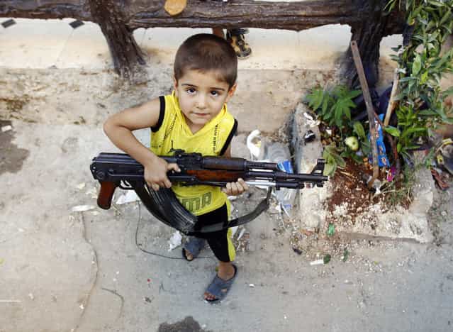 A boy plays with an AK-47 rifle owned by his father in Azaz, some 47 km (29 miles) north of Aleppo August 3, 2012. (Photo by Goran Tomasevic/Reuters)