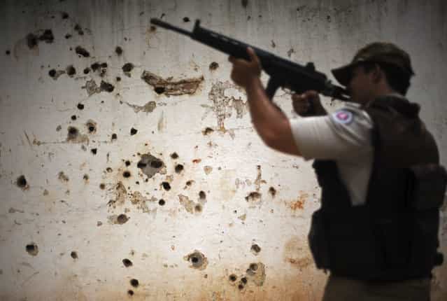 Police patrol past the [rifle wall] pockmarked by bullets from many shootouts between drug gangs and police, in the Nordeste de Amaralina slum complex in Salvador, Bahia State, March 28, 2013. One of Brazil's main tourist destinations and a 2014 World Cup host city, Salvador suffers from an unprecedented wave of violence with an increase of over 250% in the murder rate, according to the Brazilian Center for Latin American Studies (CEBELA). (Photo by Lunae Parracho/Reuters)