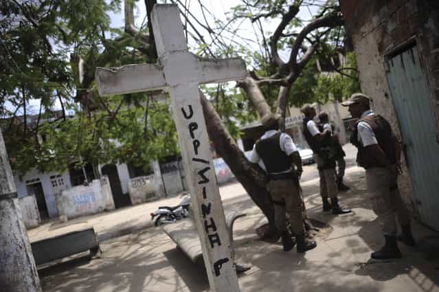 Police pause while patrolling next to a cross painted with a threat to them in the form of graffiti referring to the Community Security Base they staff in the Nordeste de Amaralina slum complex in Salvador, Bahia State, March 28, 2013. One of Brazil's main tourist destinations and a 2014 World Cup host city, Salvador suffers from an unprecedented wave of violence with an increase of over 250% in the murder rate, according to the Brazilian Center for Latin American Studies (CEBELA). Picture taken March 28, 2013. (Photo by Lunae Parracho/Reuters)