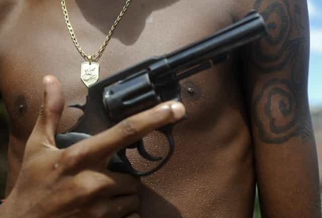 A Brazilian drug gang member nicknamed Giant, 17, poses with a gun and his medallion of St. George, in a slum in Salvador, Bahia State, April 11, 2013. One of Brazil's main tourist destinations and a 2014 World Cup host city, Salvador suffers from an unprecedented wave of violence with an increase of over 250% in the murder rate, according to the Brazilian Center for Latin American Studies (CEBELA). (Photo by Lunae Parracho/Reuters)