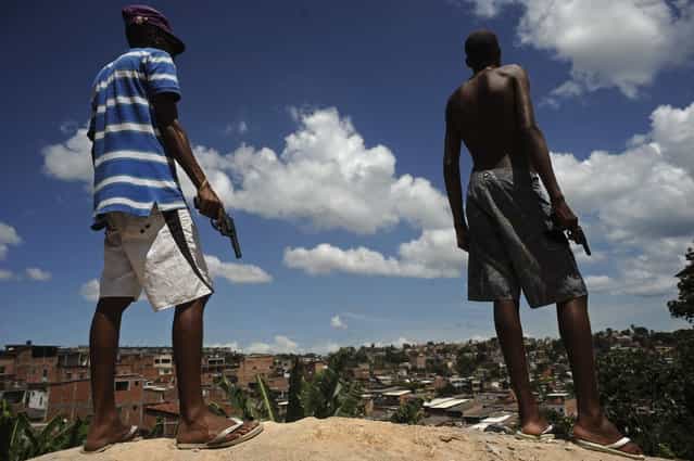 Brazilian drug gang members pose with weapons atop a hill overlooking a slum in Salvador, Bahia State, April 11, 2013. One of Brazil's main tourist destinations and a 2014 World Cup host city, Salvador suffers from an unprecedented wave of violence with an increase of over 250% in the murder rate, according to the Brazilian Center for Latin American Studies (CEBELA). (Photo by Lunae Parracho/Reuters)