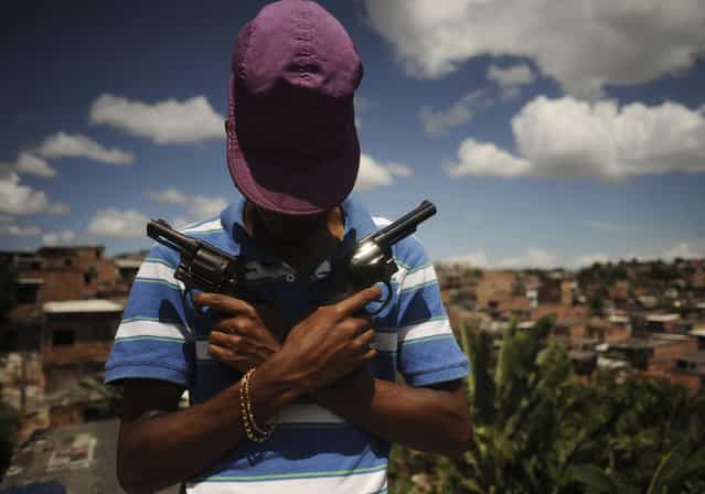 A Brazilian drug gang member nicknamed Poison, 18, poses with a gun atop a hill overlooking a slum in Salvador, Bahia State, April 11, 2013. One of Brazil's main tourist destinations and a 2014 World Cup host city, Salvador suffers from an unprecedented wave of violence with an increase of over 250% in the murder rate, according to the Brazilian Center for Latin American Studies (CEBELA). (Photo by Lunae Parracho/Reuters)