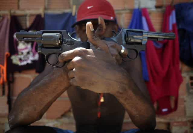 A Brazilian drug gang member nicknamed Pilintra, 26, poses with a gun atop a hill overlooking a slum in Salvador, Bahia State, April 11, 2013. One of Brazil's main tourist destinations and a 2014 World Cup host city, Salvador suffers from an unprecedented wave of violence with an increase of over 250% in the murder rate, according to the Brazilian Center for Latin American Studies (CEBELA). (Photo by Lunae Parracho/Reuters)
