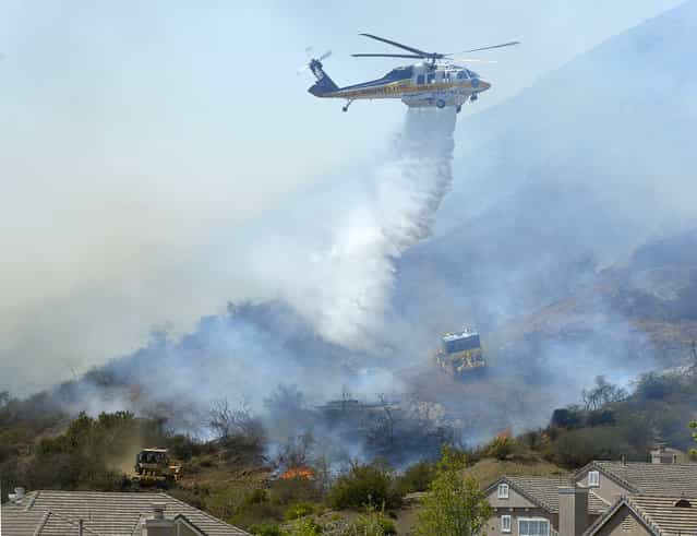 A helicopter makes a water drop on flames as earth movers clear brush along a hillside in Thousand Oaks, Calif., Thursday, May 2, 2013. A Ventura County Fire Department spokeswoman said the wildfire that broke out Thursday morning near Camarillo and Thousand Oaks, 50 miles west of Los Angeles, had spread to over 6,500 acres – more than 10 square miles – forcing evacuations of nearby neighborhoods. (Photo by Mark J. Terrill/AP Photo)