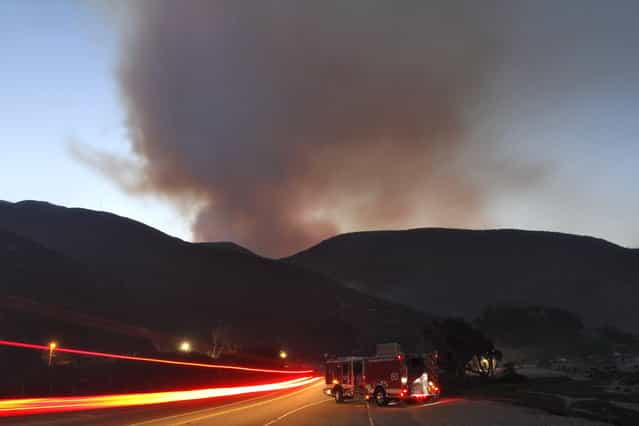 A fire engine is parked on Pacific Coast Highway as the Springs Fire burns in the hills at Point Mugu State Park, May 3, 2013. A wind-driven wildfire raging along the California coast north of Los Angeles prompted the evacuation of hundreds of homes and a university campus on Thursday as flames engulfed several farm buildings and recreational vehicles near threatened neighborhoods. (Photo by Jonathan Alcorn/Reuters)