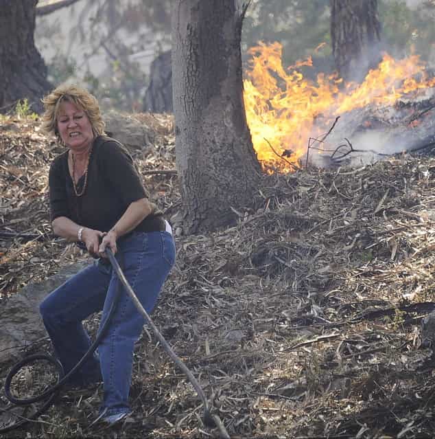 A resident pulls a hose line to attempt to stop flames from spreading down the hillside as a raging wildfire pushes towards the coast in Camarillo May 2, 2013. The wind-driven brush fire raging along the California coast north of Los Angeles prompted the evacuation of hundreds of homes and a university campus on Thursday as flames engulfed several farm buildings and recreational vehicles near threatened neighborhoods. (Photo by Gene Blevins/Reuters)