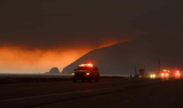 Fire department personnel drive along Pacific Coast Highway near Point Mugu as a thick layer of smoke sits overhead during a wildfire that burned several thousand acres on Thursday, in Ventura County. (Photo by Mark J. Terrill/Associated Press)