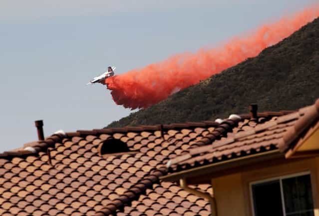 A firefighting aircraft drops fire retardant along a hill side near homes in Thousand Oaks, Calif. on Thursday, May 2, 2013. A wildfire fanned by gusty Santa Ana winds raged along the fringes of Southern California communities on Thursday, forcing evacuation of homes and a university while setting recreational vehicles ablaze. (Photo by Nick Ut/AP Photo)