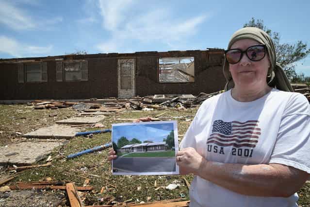 Lean Newbury holds up a picture of her father's home (rear) before it was destroyed by a tornado that ripped through the area on May 22, 2013 in Moore, Oklahoma. The tornado of at least EF4 strength and two miles wide touched down May 20 killing at least 24 people and leaving behind extensive damage to homes and businesses. U.S. President Barack Obama promised federal aid to supplement state and local recovery efforts. (Photo by Scott Olson/AFP Photo)