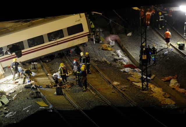 Rescuers work at the site of a train accident as the bodies of the victims, covered with blankets, lie on the ground, near the city of Santiago de Compostela on July 24, 2013. At least 35 people died and 200 people were injured when a train derailed in Galicia in northwestern Spain today, the president of the regional government of Galicia said. The train which carried 238 passengers originated in Madrid and was bound for the northwestern town of Ferrol. (Photo by Miguel Riopa/AFP Photo)