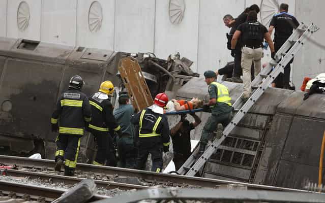 A woman is evacuated by emergency personnel at the scene of a train derailment in Santiago de Compostela, Spain, on Wednesday, July 24, 2013. A train derailed in northwestern Spain on Wednesday night, toppling passenger cars on their sides and leaving at least one torn open as smoke rose into the air. Dozens were feared dead, with possibly even more injured. (Photo by Antonio Hernandez/AP Photo/El correo Gallego)