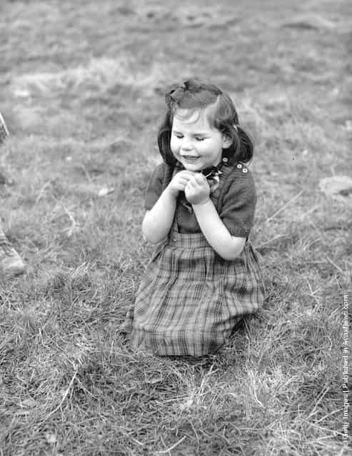 A little blind girl kneels in the grass clutching a baby chick in her hands