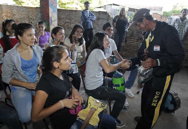 Trash recycler and craftsman Nicolas Gomez (R) greets students of the Orchestra of Recycled Instruments of Cateura, for which Gomez makes all their instruments, in Cateura, near Asuncion, May 9, 2013. The orchestra is the brainchild of its conductor Favio Chavez, who wanted to help the children of garbage pickers at the local landfill, and the instruments are made from salvaged materials by craftsman Gomez. The orchestra now involves 30 schoolchildren who have toured countries in Latin America, North America and Europe to play music ranging from Beethoven and Mozart to the Beatles and Paraguayan folk songs. (Photo by Jorge Adorno/Reuters)