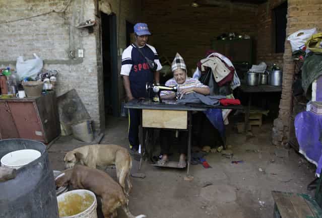 Trash recycler and craftsman Nicolas Gomez (L) watches as his wife Natividad Romero sews clothes from cloth recovered from the local landfill, at their home in Cateura, near Asuncion, May 9, 2013. The Orchestra of Recycled Instruments of Cateura is the brainchild of its conductor Favio Chavez, who wanted to help the children of garbage pickers at the local landfill, and the instruments are made from salvaged materials by craftsman Gomez. The orchestra now involves 30 schoolchildren who have toured countries in Latin America, North America and Europe to play music ranging from Beethoven and Mozart to the Beatles and Paraguayan folk songs. (Photo by Jorge Adorno/Reuters)