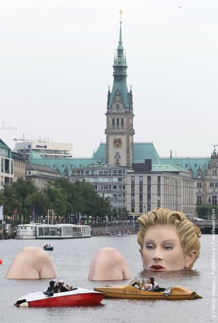 People in boats approach Die Badende (The Bather), a giant sculpture showing a womans head and knees as if she were resting in the Binnenalster lake in Hamburg, Germany