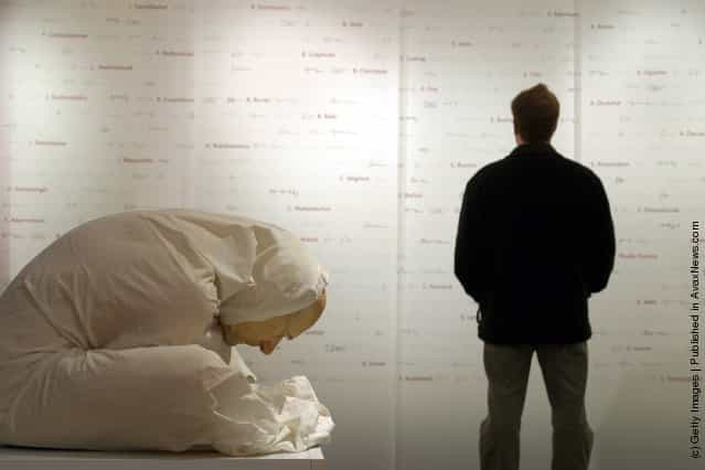 A man views a wall listing the known names of 800 out of an estimated 10,000 victims of Nazi experiments as a a memorial entitled Man with Sheet created by Australian artist Ron Mueck crouches silently as a testiment to the medical professions shame at the Medical History Museum