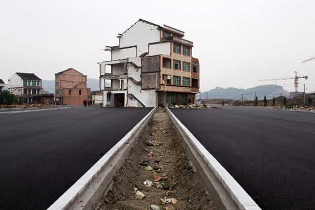 This picture taken on November 22, 2012 shows a half-demolished apartment building standing in the middle of a newly-built road thanks to a Chinese couple that refused to move in Wenling, in eastern China's Zhejiang province. Luo Baogen, 67, and his 65-year-old wife have waged a four-year battle to receive more than the 41,300 USD compensation offered by the local government of Daxi, a Chinese newspaper said. The phenomenon is called a [nail house] in China, as such buildings stick out and are difficult to remove, like a stubborn nail. (Photo by STR/AFP Photo)